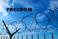 Barbed wire against the blue sky and white clouds. The inscription in black - freedom. The concept of freedom, human Royalty Free Stock Photo