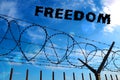 Barbed wire against the blue sky and white clouds. The inscription in black - freedom. The concept of freedom, human Royalty Free Stock Photo