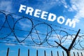 Barbed wire against the blue sky and white clouds. The inscription is blurred in white - freedom. The concept of freedom Royalty Free Stock Photo