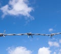 Barbed wire against summery sky of blue with clouds. Freedom, prison, escape concept background. Royalty Free Stock Photo