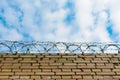 Barbed wire on a brick wall against a blue sky with clouds. Royalty Free Stock Photo