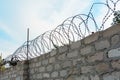 Barbed wire on brick wall or fence in front of blue sky. Concept of security and safe or restriction of liberty and freedom.