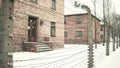 Barbed wire fence of Auschwitz Birkenau concentration camp. Old brick buildings in falling snow Royalty Free Stock Photo