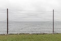 Barbed wire on high steel fence on blue sky and sea background