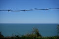 Barbed wire mesh fence on seashore at evening. Concept of freedom. A barbed wire fence with a view on blue sea or ocean. green Royalty Free Stock Photo