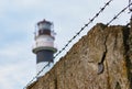 barbed wire and stone fence, behind them a lighthouse. concept of slavery, dictatorship and totalitarianism