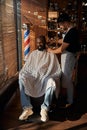 Barber in apron shaving client beard in barbershop Royalty Free Stock Photo