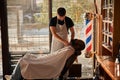 Barber in apron trimming client beard in barbershop Royalty Free Stock Photo