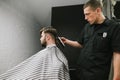 Barber cuts the client hair clipper in a men`s hairdresser. Hairdresser creates stylish hairstyle for bearded client. Man doing Royalty Free Stock Photo