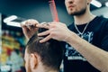 Tattooed Barber cuts the hair of the client with scissors. Close up. Attractive male is getting a modern haircut in Royalty Free Stock Photo