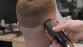 Barber cuts red-haired client with trimmer in barbershop