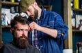 Barber in denim jacket busy with trimming hipster, barbershop background. Client with beard and mustache covered with