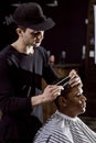 The barber dressed in black clothes is cutting a man`s hair holding scissors and comb in his hands in a barbershop Royalty Free Stock Photo