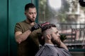 Barber dries hair and makes a styling of dark-haired man at a barbershop
