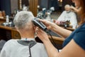 Perfect work. Barber girl using hair clipper. Making new haircut for elegant mature man sitting in armchair in the front