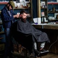 Barber with hair clipper works on haircut of bearded guy barbershop background. Hipster client getting haircut. Barber