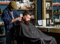 Barber with hair clipper works on haircut of bearded guy, retro barbershop background. Hipster hairstyle concept