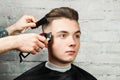 Barber hair styling of young guy in the barbershop on brick wall background, hairdresser makes hairstyle for a young man. Royalty Free Stock Photo