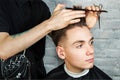 Barber hair styling of young guy in the barbershop on brick wall background, hairdresser makes hairstyle for a young man. Royalty Free Stock Photo