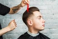 Barber hair styling of young guy in the barbershop on brick wall background, hairdresser makes hairstyle for a young man. Royalty Free Stock Photo