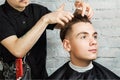 Barber hair styling of young guy in the barbershop on brick wall background, hairdresser makes hairstyle for a young man. Royalty Free Stock Photo