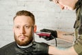 Barber hand in gloves cut hair and shaves adult gihger bearded man on a brick wall background. Close up portrait of a guy