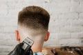 Barber hand in gloves cut hair and shaves young man on a brick wall background. Close up side portrait of a guy, back view