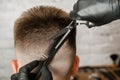 Barber hand in gloves cut hair and shaves young man on a brick wall background. Close up side portrait of a guy, back view