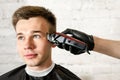 Barber hand in gloves cut hair and shaves young man on a brick wall background. Close up portrait of a guy