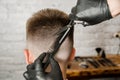 Barber hand in gloves cut hair and shaves young man on a brick wall background. Close up side portrait of a guy, back view