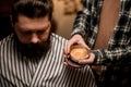 barber holds round jar of hair styling gel near the head of male client.