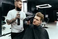 Barber makes hair styling with hair spray after haircut at the barber shop. Young handsome Caucasian man getting a Royalty Free Stock Photo