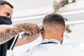 Barber with mask cutting the hair of a client using a electric shaving machine