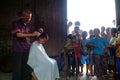 Barber providing a hair cut to a customer while a group of children watch in curiosity