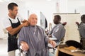 Barber putting on hairdresser cloak to elderly male client