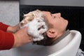 The barber's hands wash the hair and head of the hairdresser's client with foam in the sink before cutting the hair