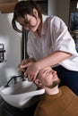 Barber shampooing washing a male clients head in the sink.