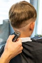 Barber shaves the temple with a cordless trimmer during a short haircut on the sides of the head. Royalty Free Stock Photo