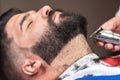 Barber shaving the beard of a handsome bearded man with an electric razor at the barber shop. Royalty Free Stock Photo