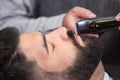 Barber shaving the beard of a handsome bearded man with an electric razor at the barber shop. Royalty Free Stock Photo