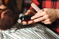 Barber shearing beard to man in barbershop, close up. Confident man visiting hairstylist in barber shop. Beard grooming
