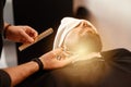 A barber stylist trims the beard of a Caucasian man, whose face is covered with towel, with scissors Royalty Free Stock Photo