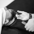 A barber stylist trims the beard of a Caucasian man, whose face is covered with towel, with scissors Royalty Free Stock Photo