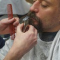 Barber trimming bearded man with shaving machine in barbershop. Hairstyling process. Haircut concept