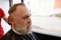Barber trimming and cutting bearded man with shaving machine in barbershop. Hairstyling process
