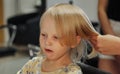 Barber woman make fashionable pretty hairstyle for cute little blond girl