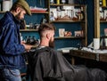 Barbershop concept. Barber with hairdryer blows off hair out of cape. Hipster bearded client got hairstyle. Barber with Royalty Free Stock Photo