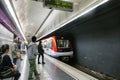 Barcelona metro station tunnel with people seated and standing waiting train stop sign in fore