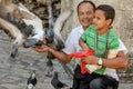 Barcelona / Spain - Oct./2018: Adult latin man with a boy on knees feeds the pigeons on the city street. Happy life, family values