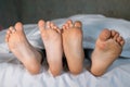 bare, clean feet of two children, offspring, lying side by side under the same blanket on the bed
